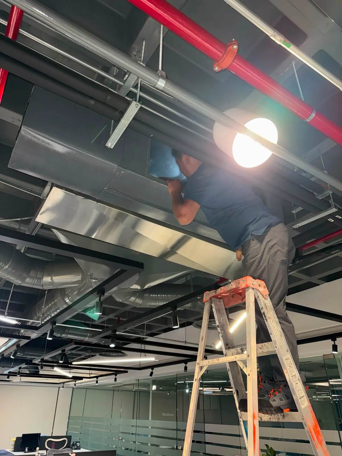 Técnico ajustando canalización en plafón industrial expuesto sobre escalera