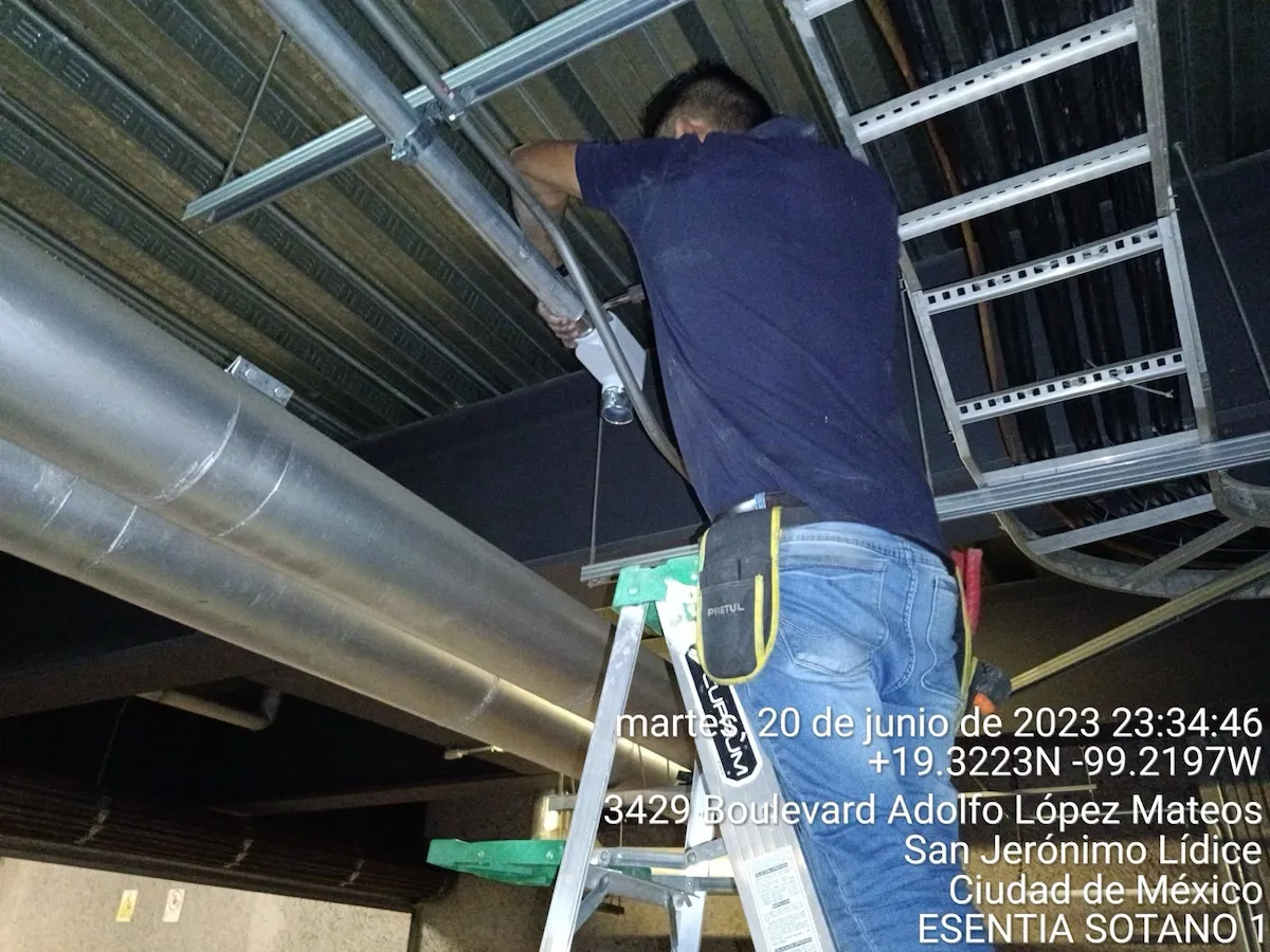 Técnico ajustando tubería metálica y cámara CCTV bajo escalerilla en Sótano 1