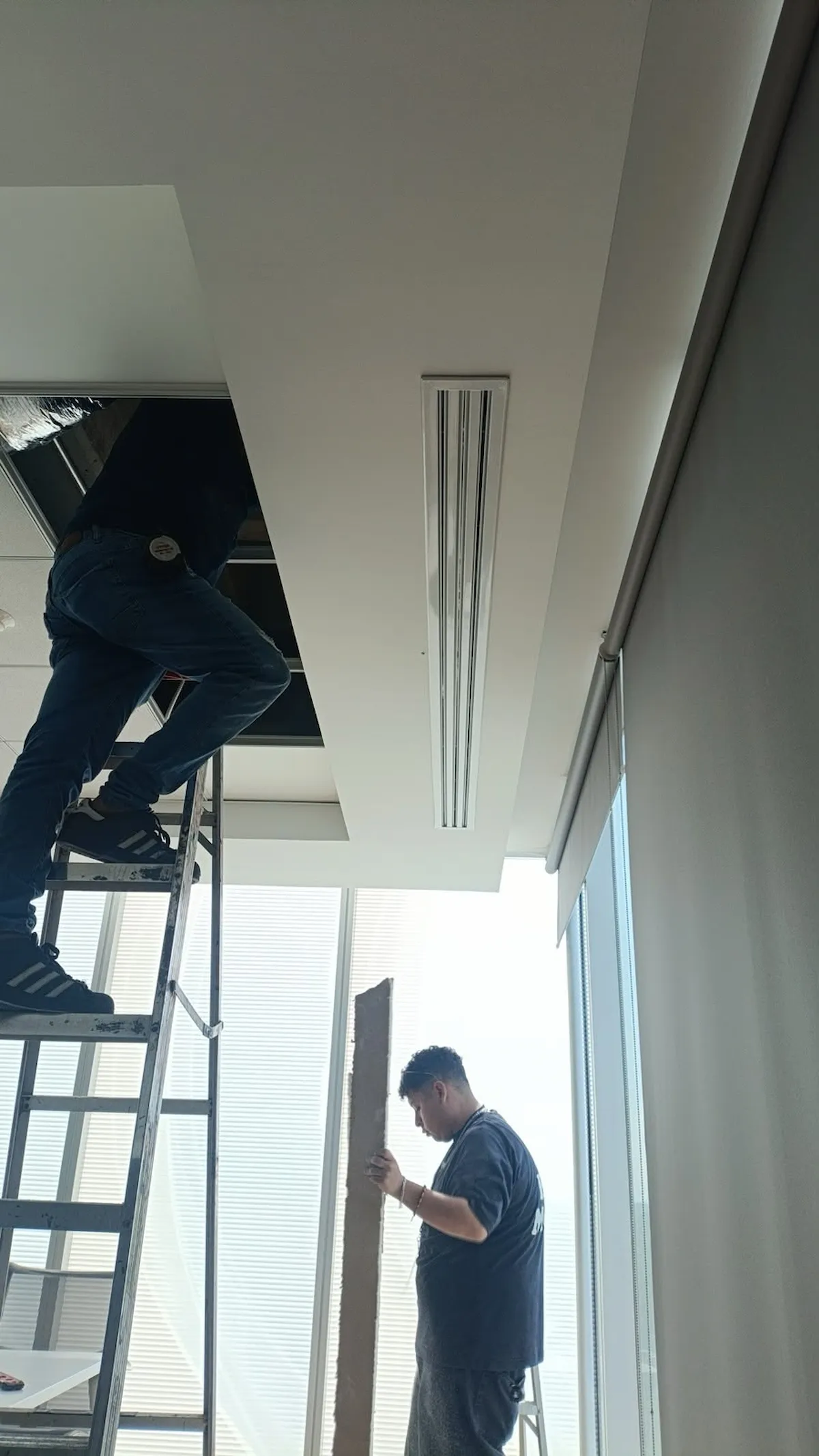 Técnico accediendo al plafón modular desde escalera para inspección de cableado